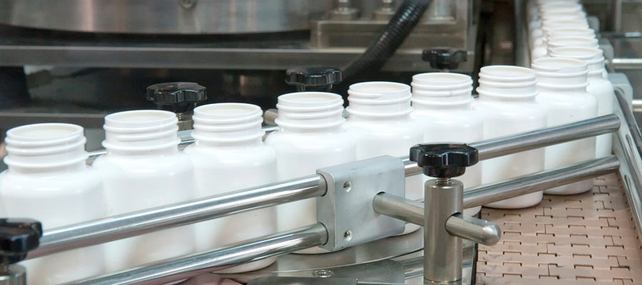 White supplement bottles on the conveyor belt of a high-speed packaging machine.