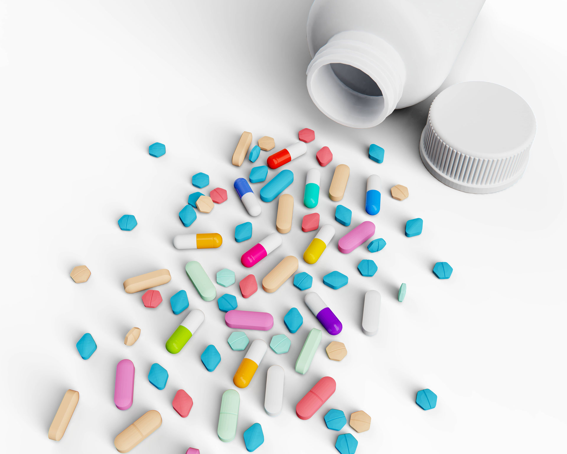 Colorful tablets and capsules spread out on a surface next to an white vitamin bottle laying on its side.