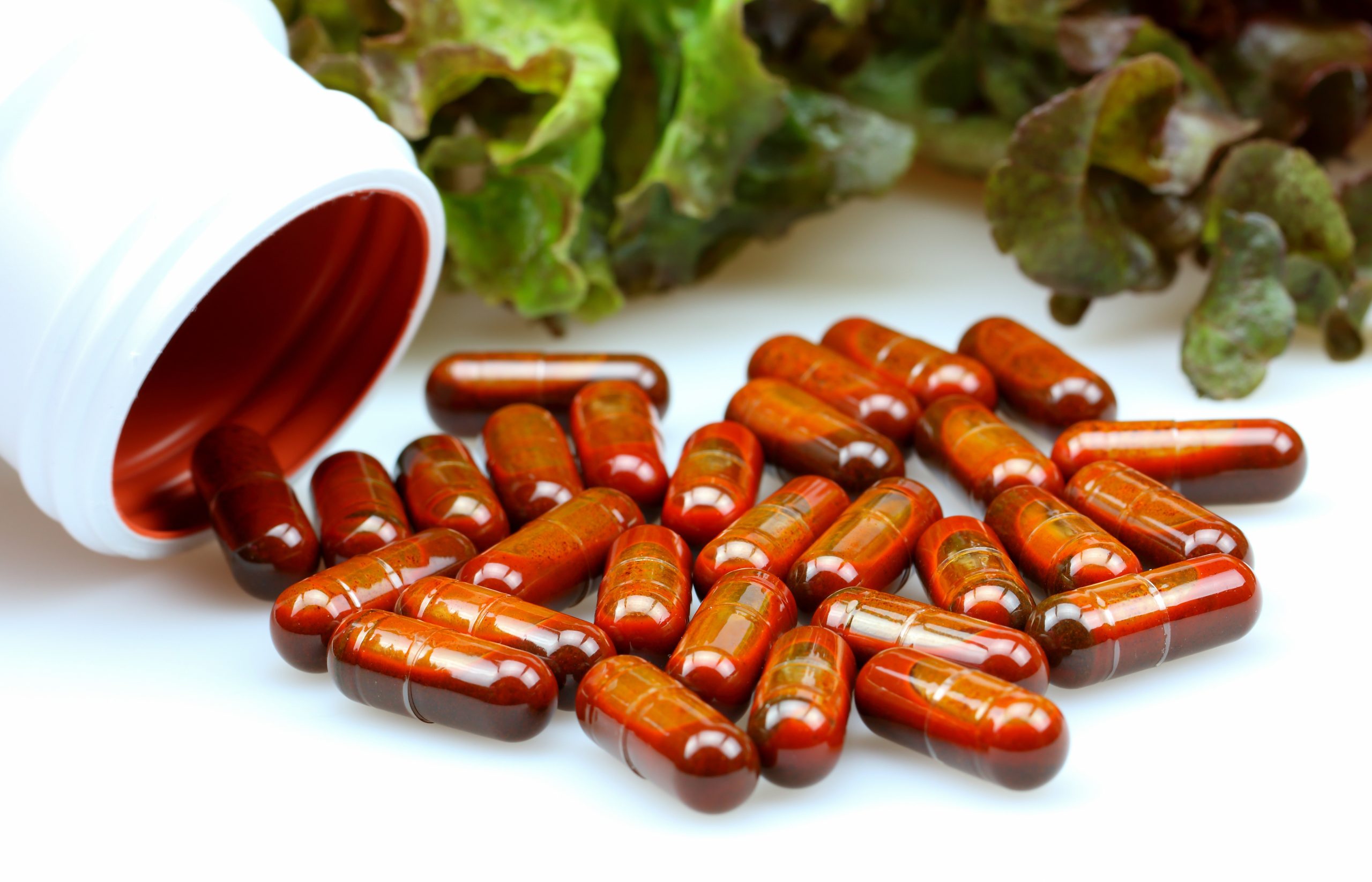 Bright orange capsules spilling out of a white bottle turned on its side.