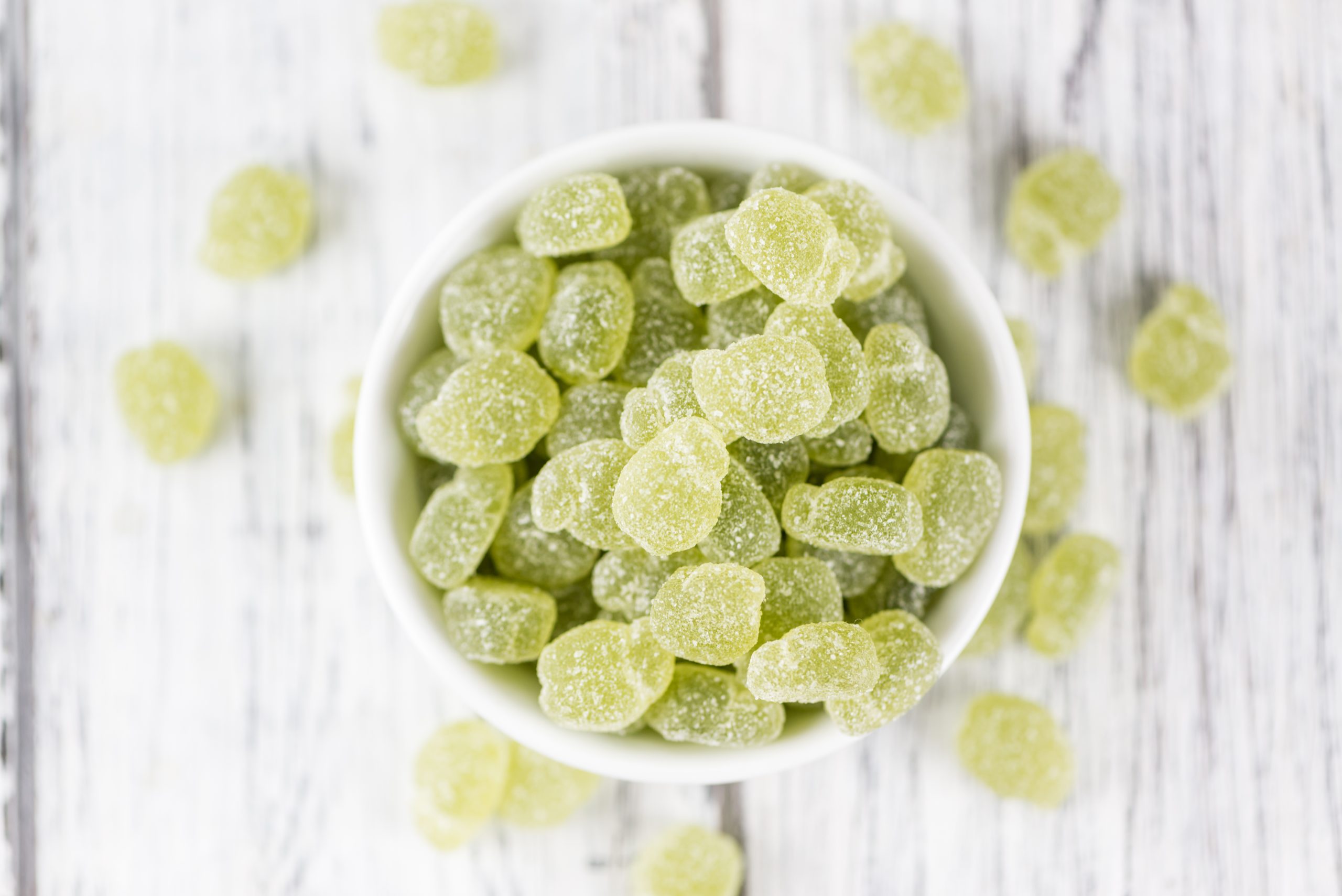 Closeup of bright green gummy supplements overflowing in a large white bowl.