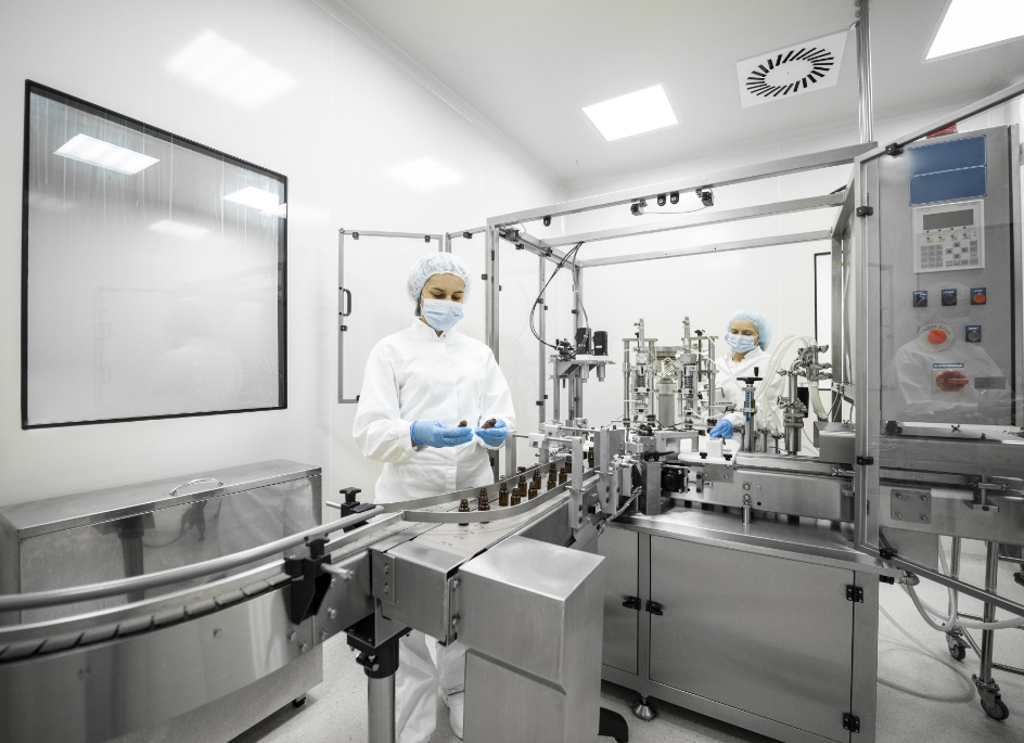 Two women wearing PPE inspect nutraceutical products coming off of a production line.