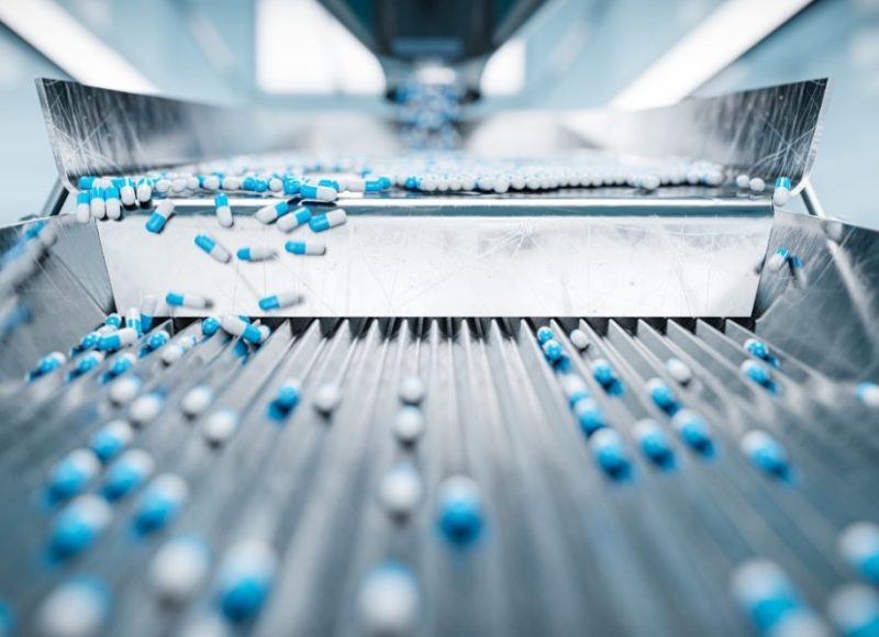 Hundreds of blue and white capsules moving down a manufacturing line.