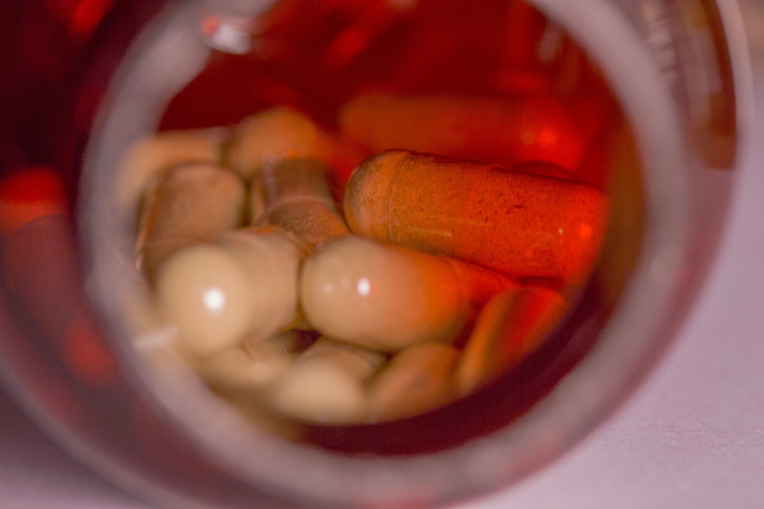 Closeup of tan herbal supplements inside of a red plastic bottle.