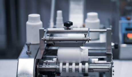 Packaging and labeling machine labeling a white supplement bottle.