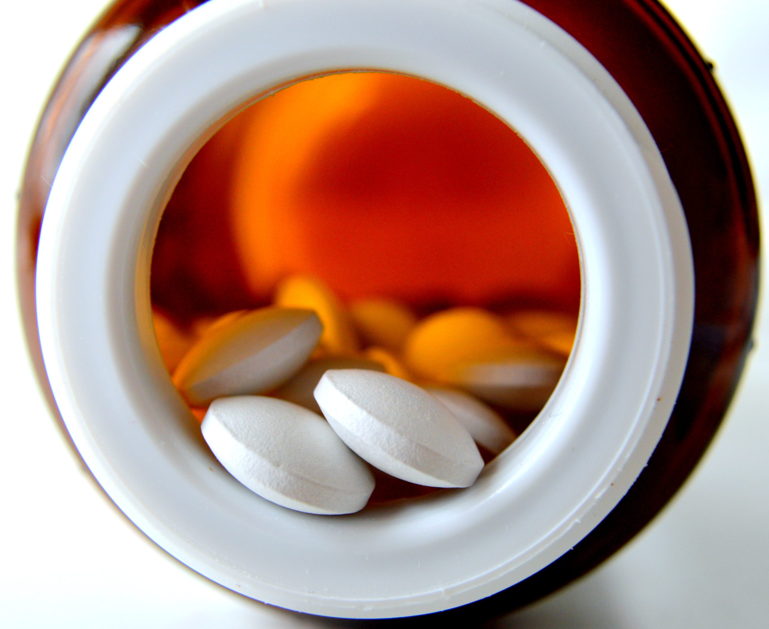 Closeup of white vitamins in an orange vitamin bottle.