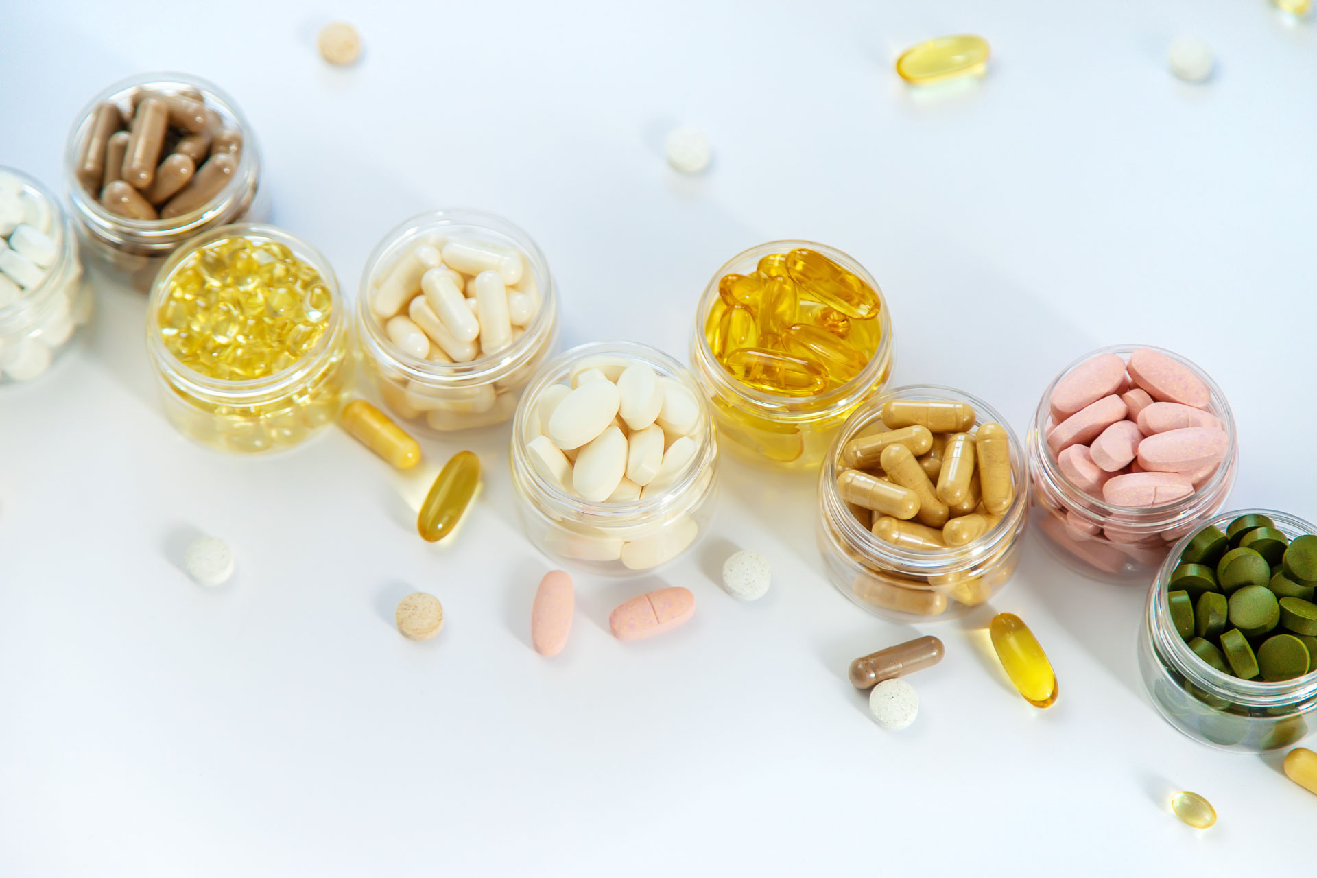 Clear glass jars filled with various nutraceuticals arranged on a white table in a diagonal pattern.