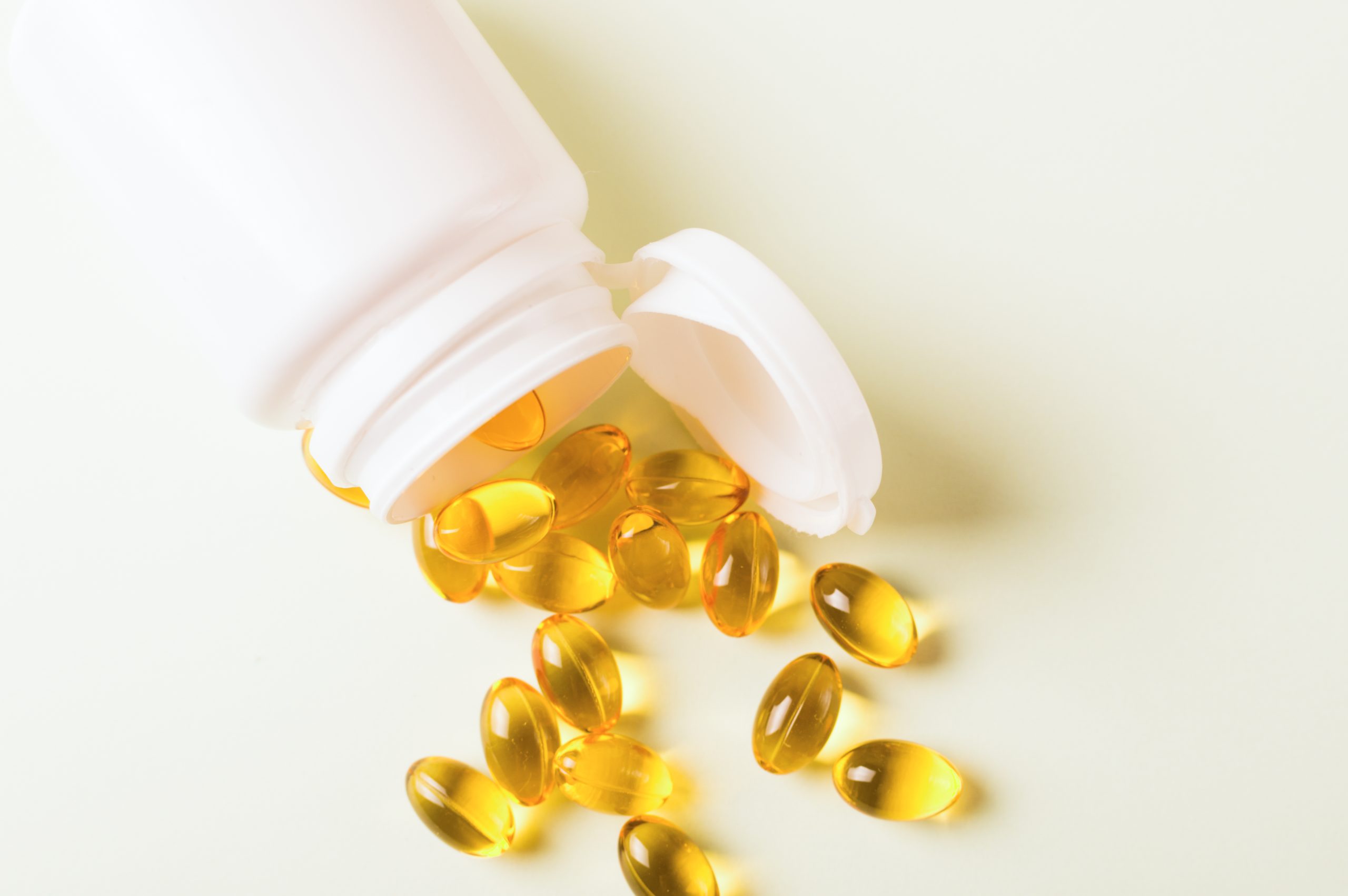 Bright yellow softgel capsules spilling out of an overturned white bottle.